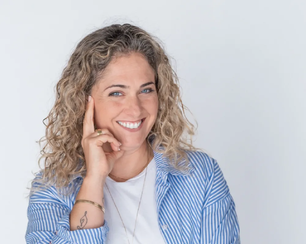 דנה עם חיוך ואצבע לצד הפנים בתנוחת חשיבה